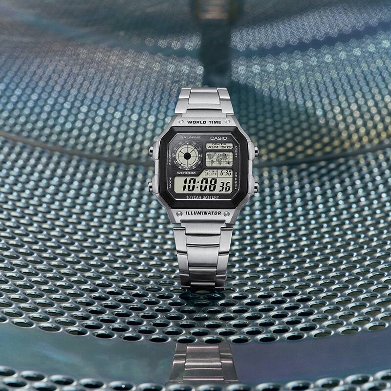 Il s'agit d'une photo de la G-SHOCK AE-1200WHD-1AV placée sur une surface métallique dans une laverie automatique.
