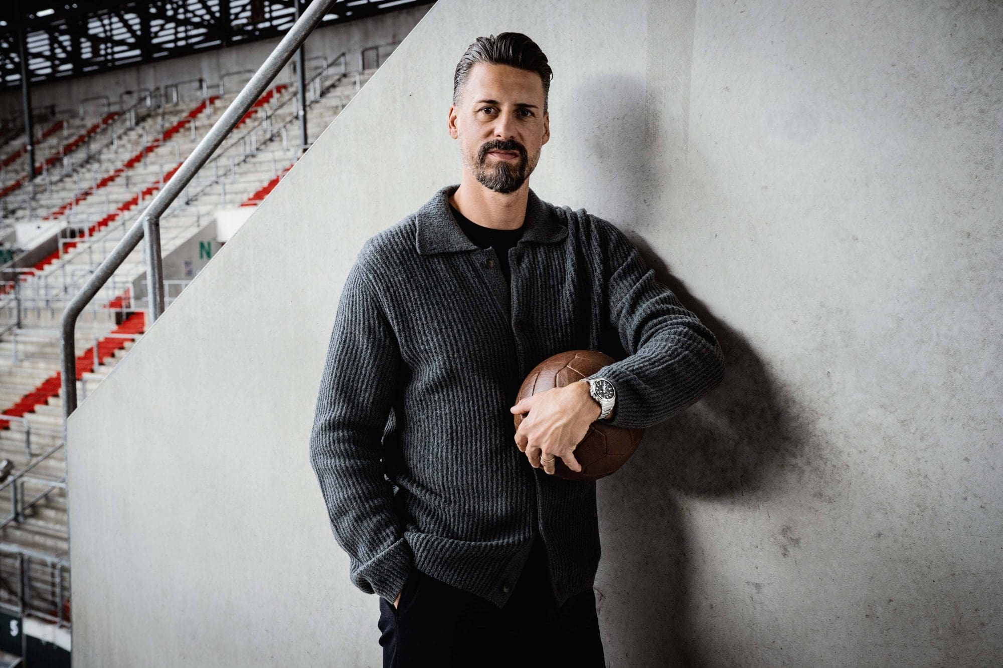 Sandro Wagner steht im leeren Stadion und trägt die GST-B1000.