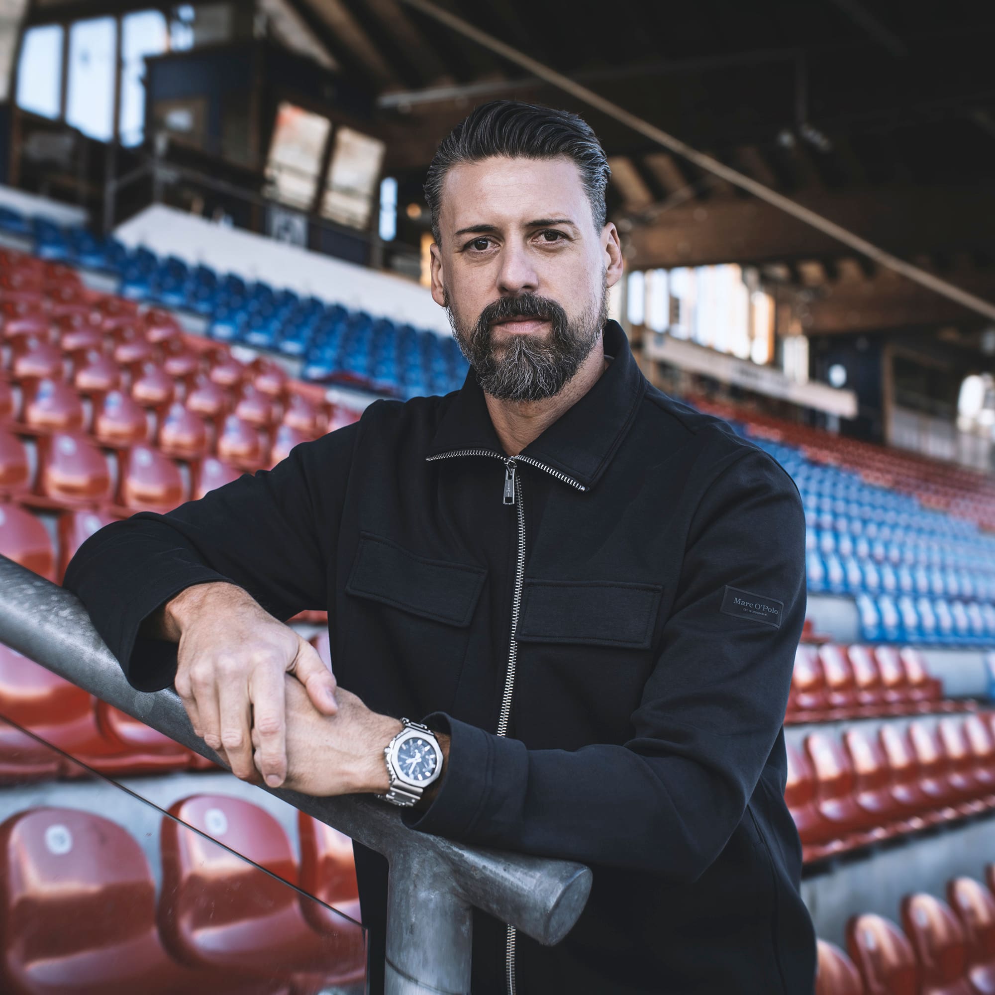 Sandro Wagner lehnt sich am Geländer auf einer Tribüne an, er trägt dabei die GM-2110 Armbanduhr von G-SHOCK