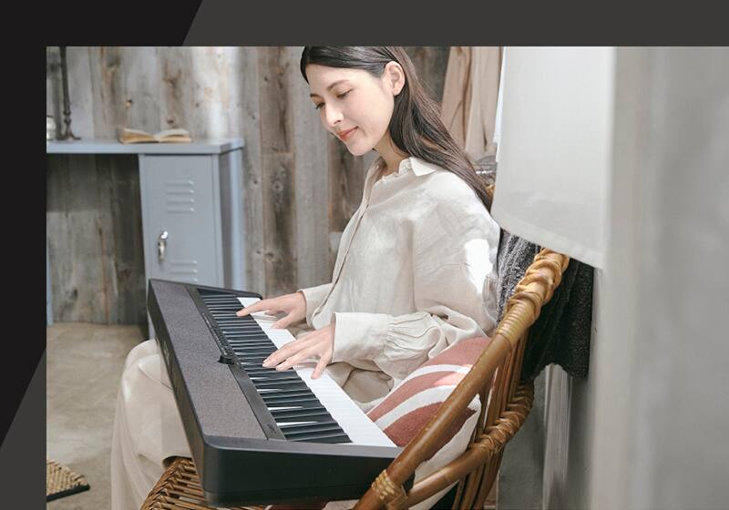 Eine Frau sitzt auf einem Korbstuhl und spielt auf dem schwarzen Casiotone CT-S1-76, das auf ihrem Schoß liegt