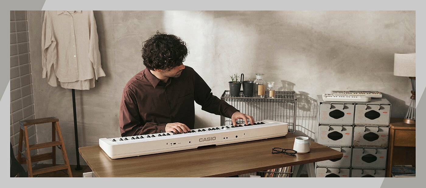 Ein Mann sitzt in einem hellen Raum an einem Schreibtisch und spielt auf dem weißen Casiotone CT-S1-76