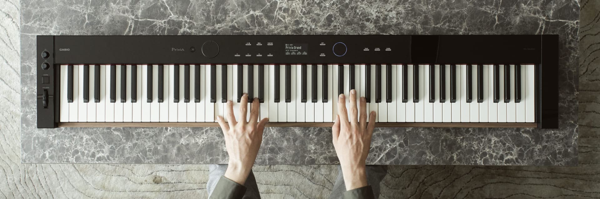 Zwei Hände spielen das schwarze Privia PX-S6000 Keyboard auf einem Tisch.