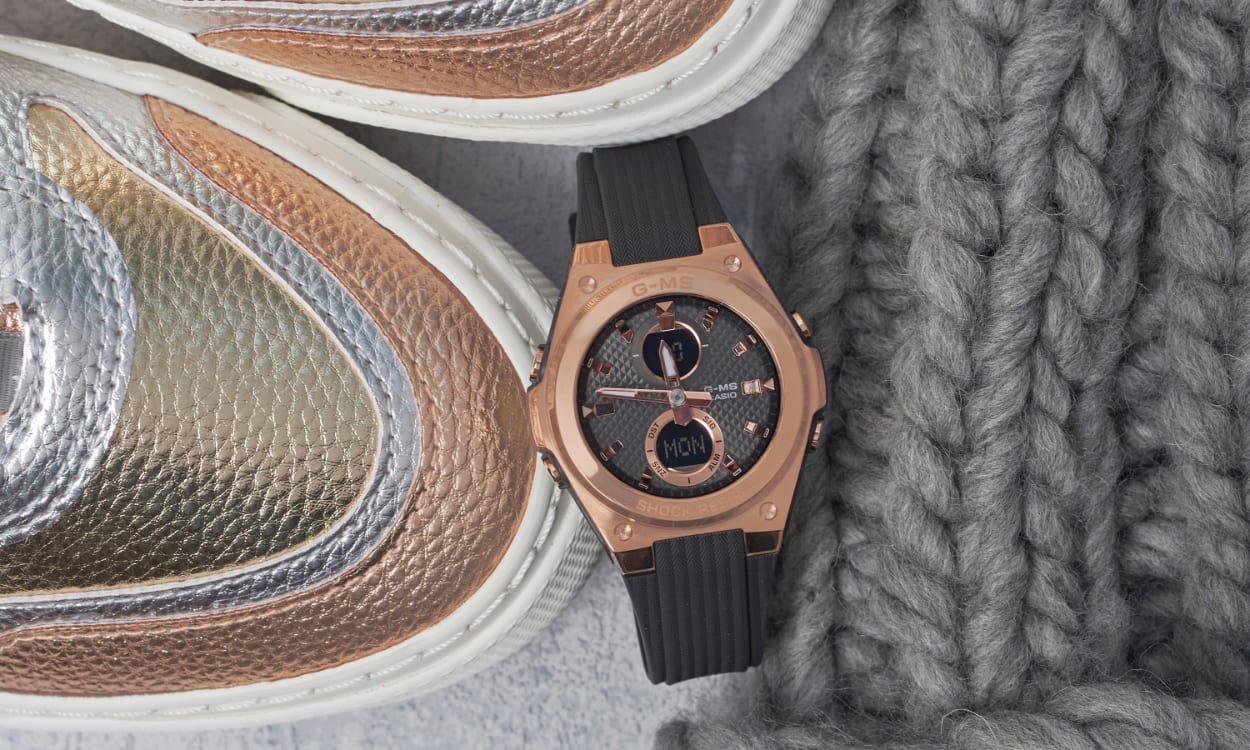 Die schwarz-rosé goldene MSG-C100G-1AER liegt neben Sneakern und einer Decke auf dem Boden.