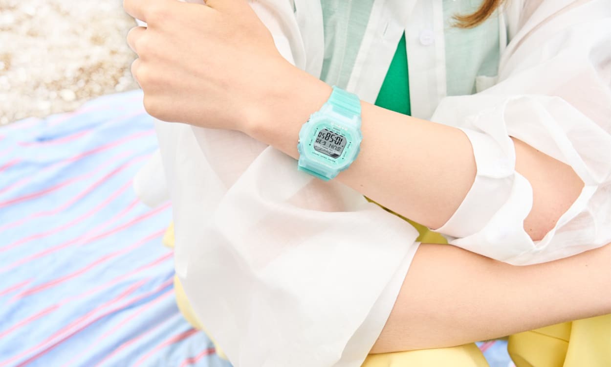 Close-Up: Die Baby-G BGD-565S-2ER in türkis an einem Handgelenk, im Hintergrund ist eine Decke auf Sandstrand zu sehen.