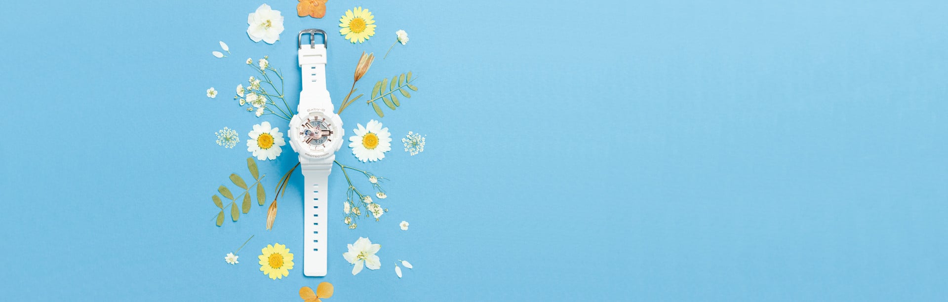 Die weiße BA-110 von Baby-G liegt neben Blumen auf einem blauen Hintergrund.