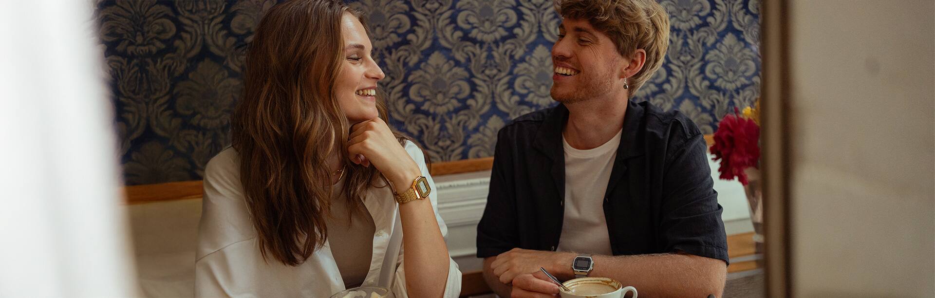 Eine Frau und ein Mann tragen die ABL-100 in verschiedenen Farben und lächeln sich verliebt in einem Café an.