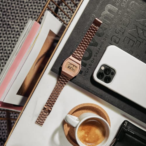 Aktuelle Casio Vintage Uhr in rosé mit Digitalanzeige neben einem iPhone, Kaffeetasse und Magazinen