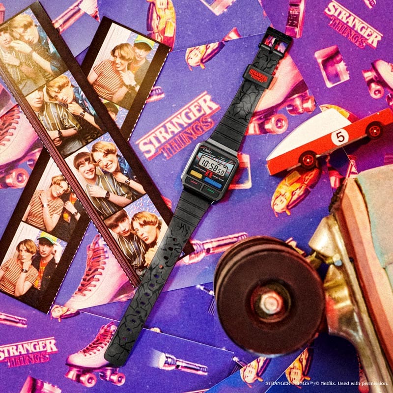 Die Stranger Things und Casio Vintage Collection Kollaborationsuhr auf einem Tisch mit Fotos aus einem Fotoautomaten und mehreren Stranger Things - Stickern