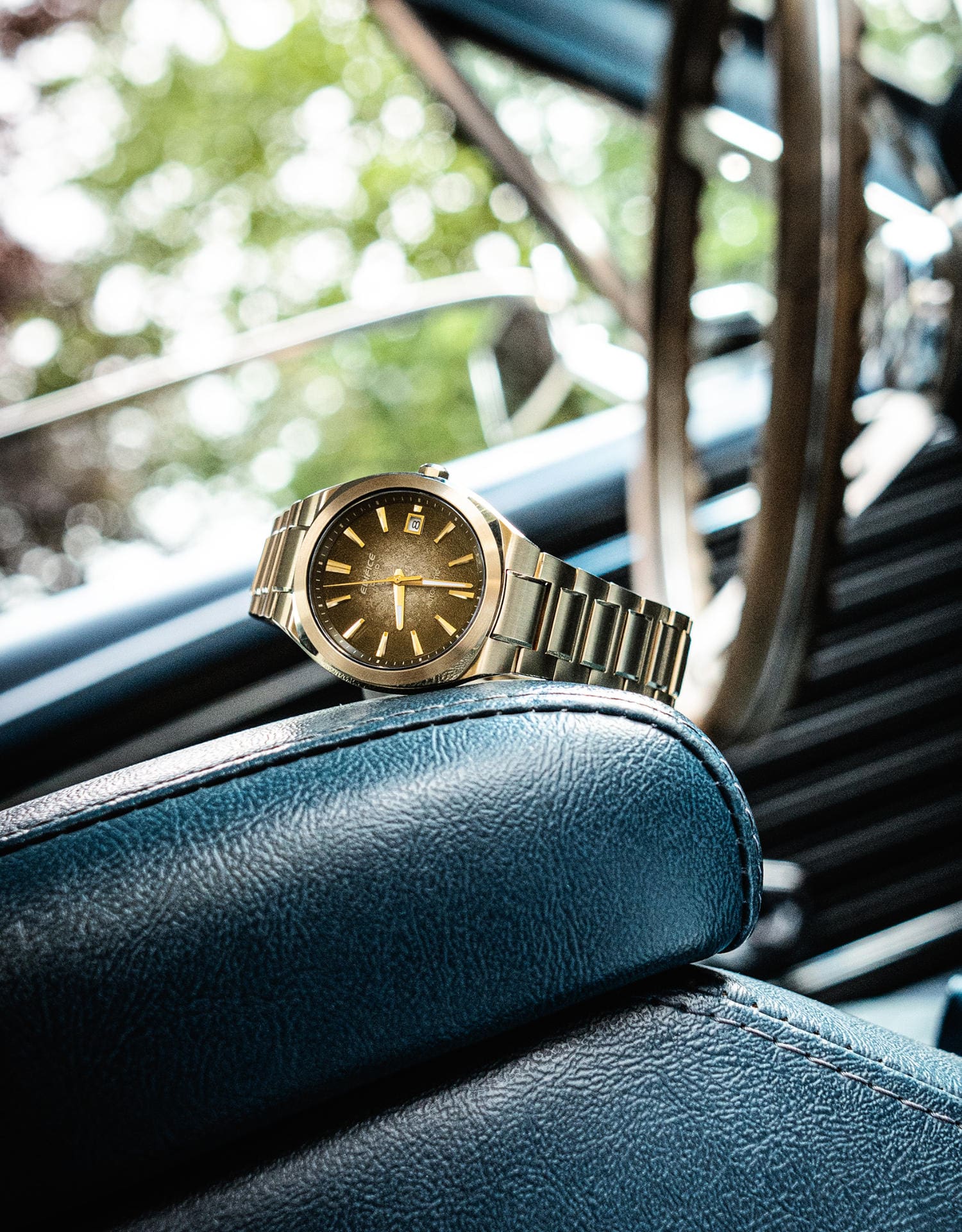 Die goldene Automatikuhr EFK-200 mit braunschimmerndem, analogem Zifferblatt auf einem Ledersitz im Auto.