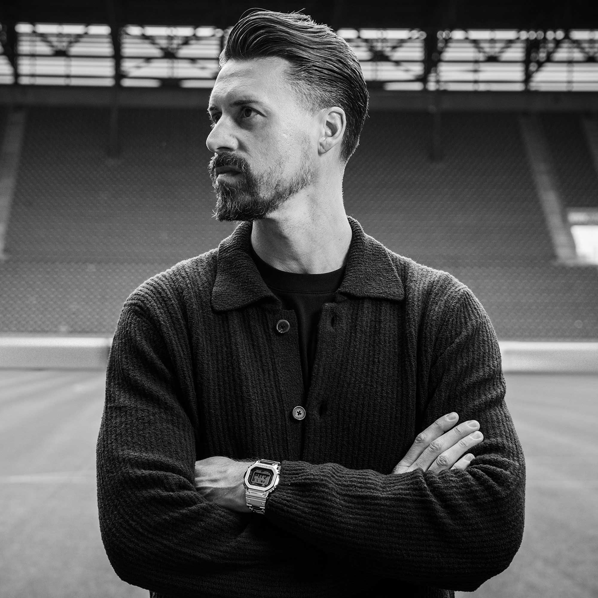 Schwarz-weiß Aufnahme von Sandro Wagners seitlichem Profil der mit verschränkten Armen zur Seite schaut und die GMW-B5000D trägt.