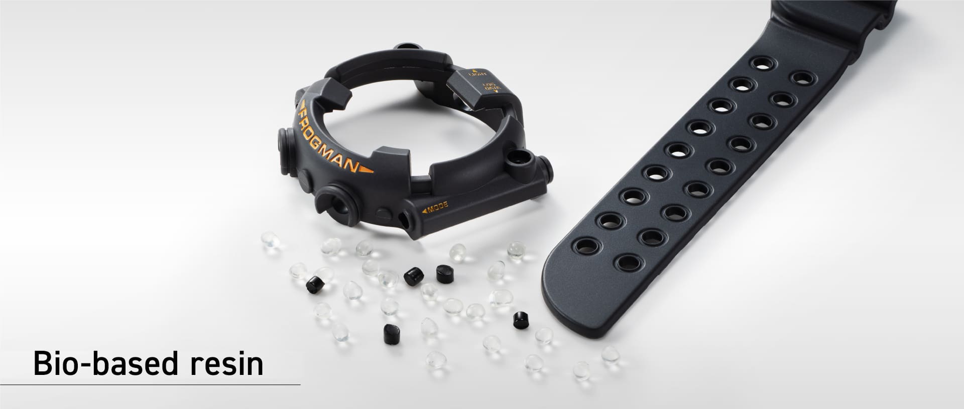 Das schwarze Gehäuse und Armband einer G-SHOCK Uhr liegen neben Pellets aus biobasiertem Resin.