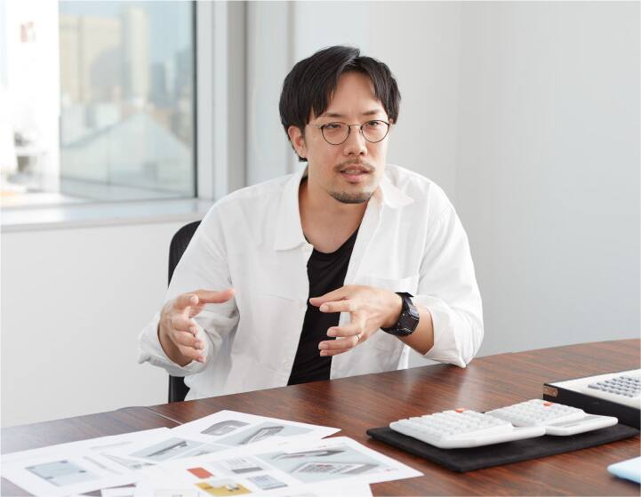 Der Produktdesigner Shunsuke Oka sitzt an seinem Schreibtisch und erklärt die vor ihm liegenden ergonomischen Rechner
