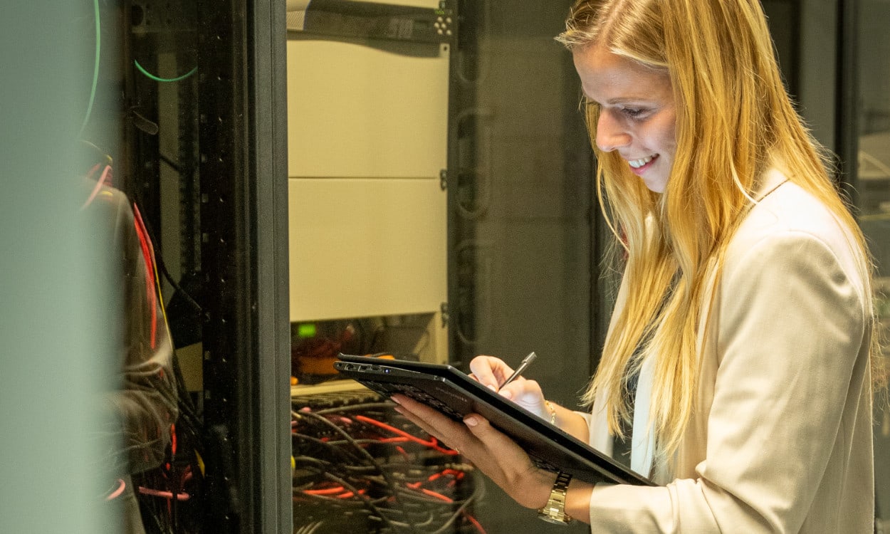 Eine Mitarbeiterin aus der IT-Abteilung steht mit einem Tablet am Server