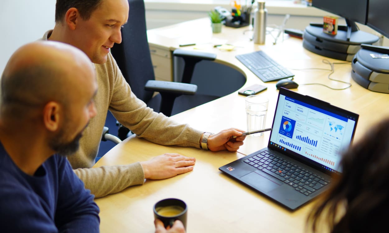 Drei Mitarbeitende aus dem Digital Marketing besprechen aktuelle Zahlen, die auf einem Laptop zu sehen sind.