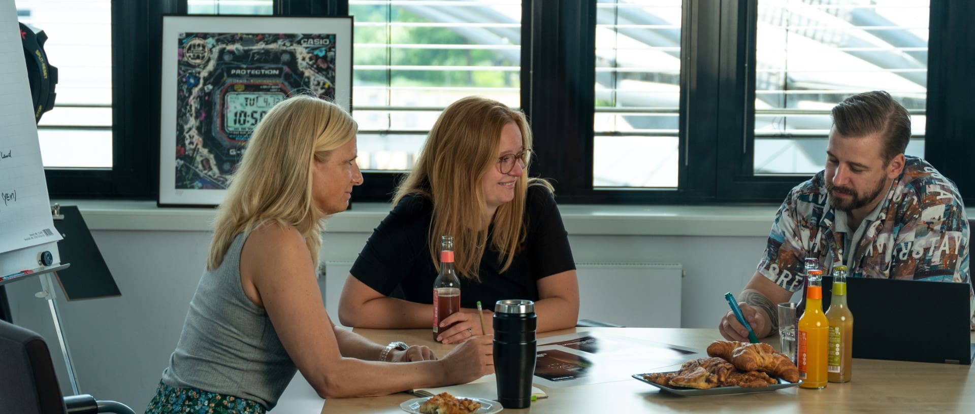 Drei Personen aus dem Brand-Marketing Team sitzen im Konferenzraum am Tisch und besprechen neue Designs.