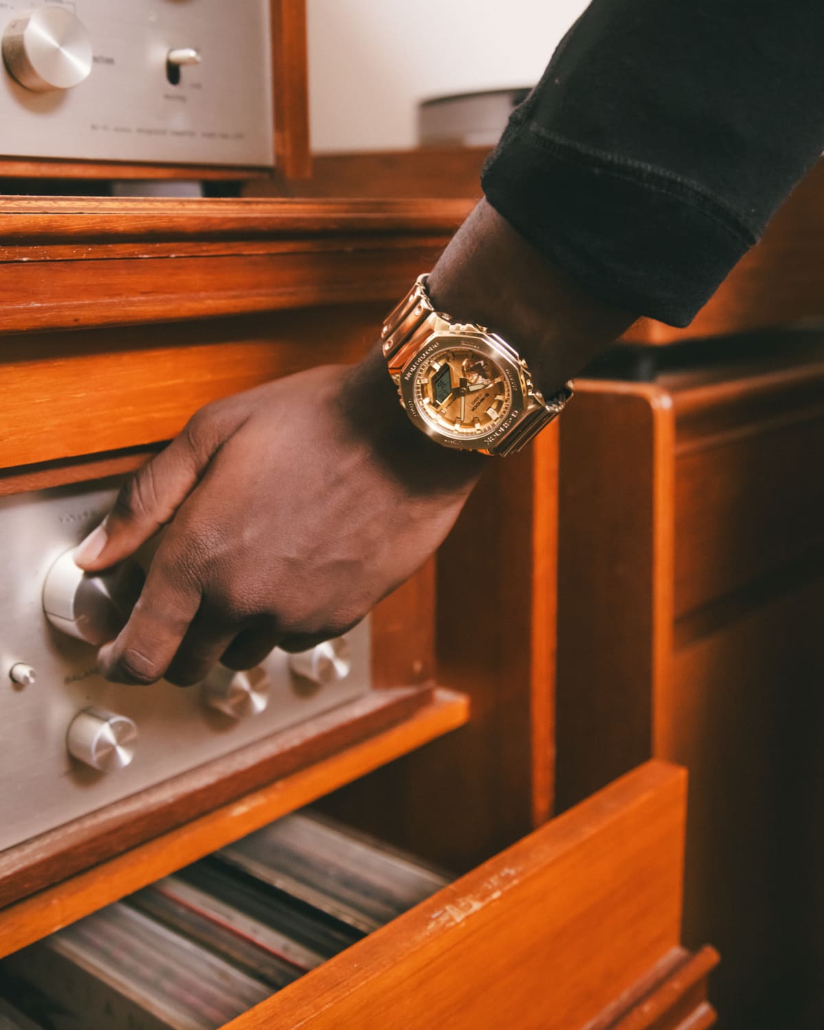 Das goldfarbene G-Shock Fine-Metall-Modell GM-2100YMG-9A am Handgelenk eines Mannes, der am Knopf eines Plattenspielers dreht.