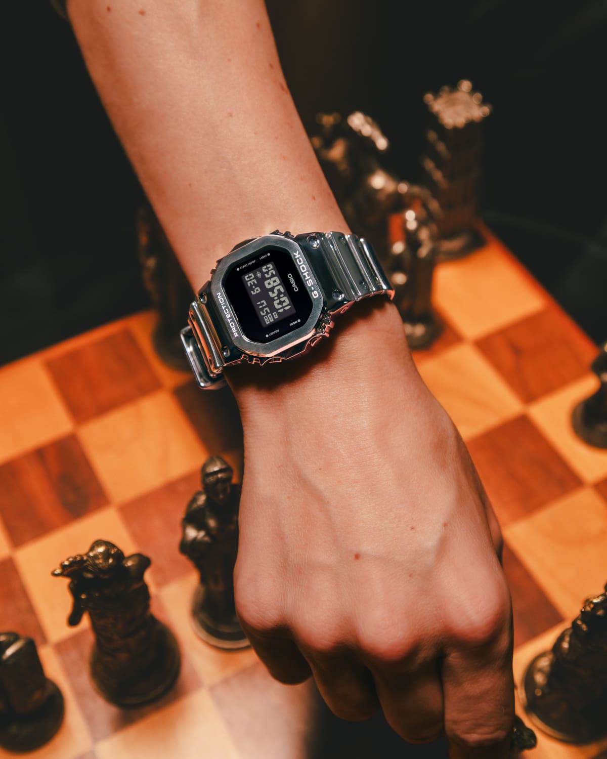 Das silberfarbene G-Shock Fine-Metall-Modell GM-5600YM-8 an einem Handgelenk  über einem Schachbrett