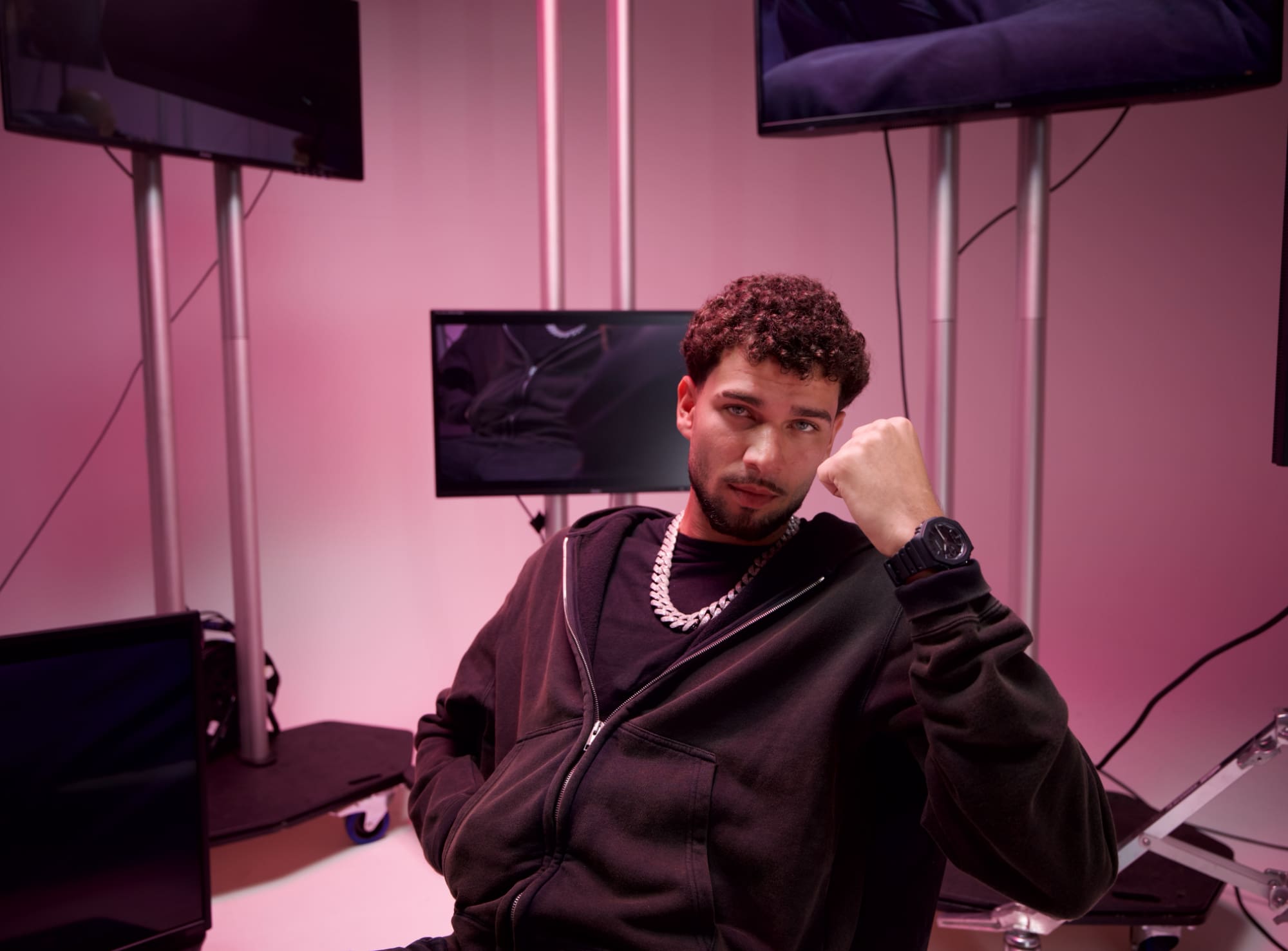 Lucio101 trägt die G-SHOCK GA-2100LXB-1A und sitzt vor einem pinken Hintergrund mit mehreren Monitoren und blickt in die Kamera.