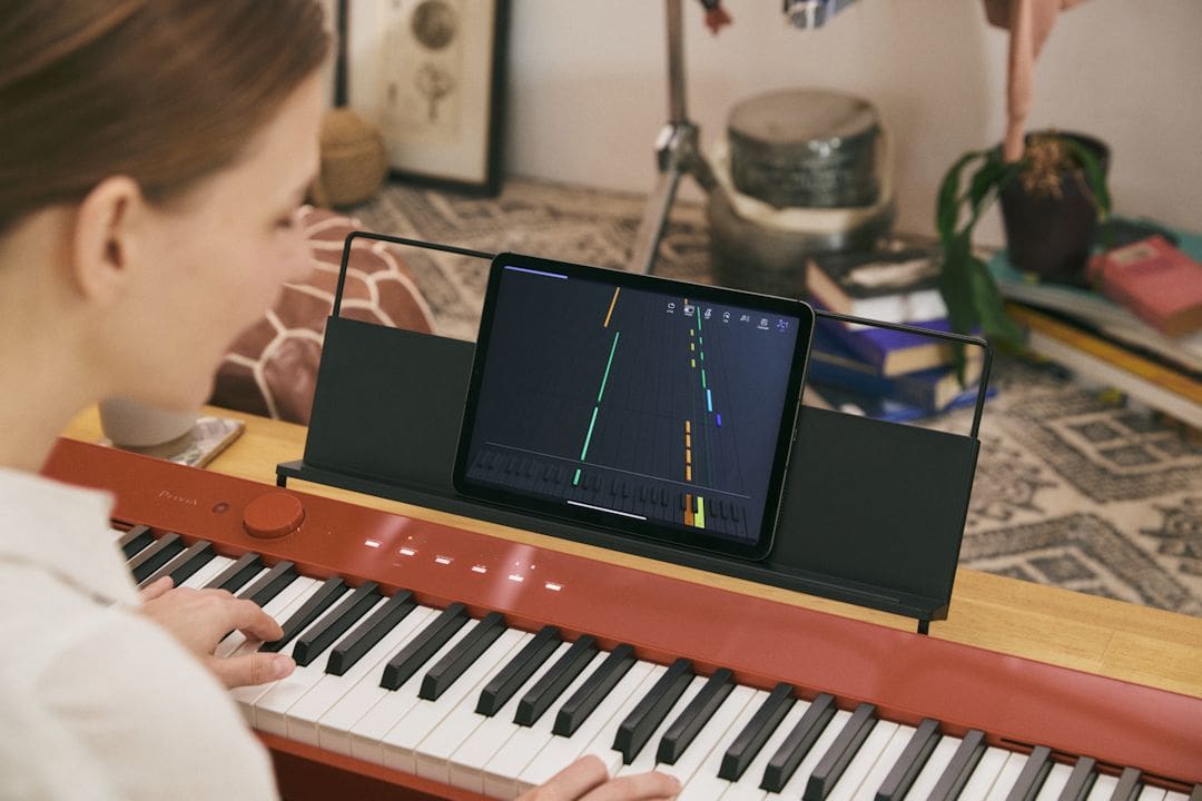 Eine Person sitzt an einem roten CASIO E-Piano und spielt klavier. Auf dem Notenständer steht ein Tablet, das eine digitale Klaviatur mit farbigen Linien und Symbolen anzeigt.