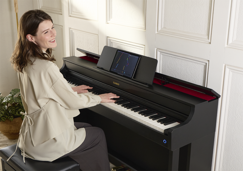 Eine Frau, die auf einem schwarzen Digitalpiano spielt, während die App auf einem Tablet angezeigt wird.