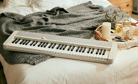 Das weiße CT-S1WE Digitalpiano liegt auf einem Bett