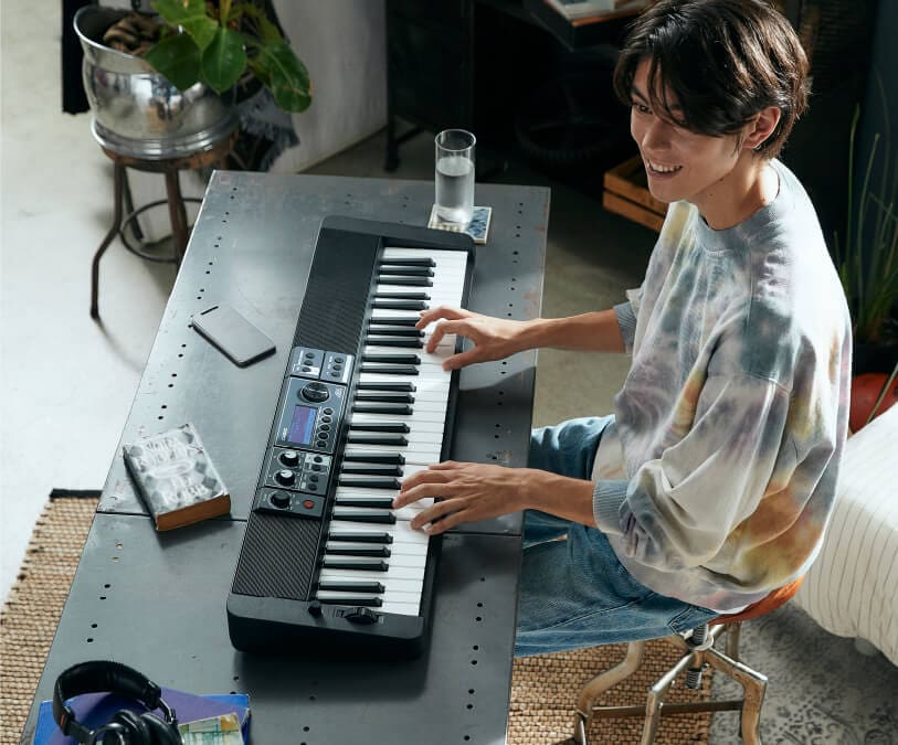 Ein junger Mann spielt gut gelaunt auf einem Casiotone CT-S500, dass in einem Wohnraum auf einem Tisch liegt