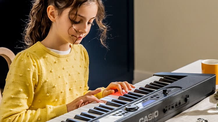 Ein Mädchen sitzt an einem Tisch und spielt auf dem Casiotone LK-S450 Digitalpiano.