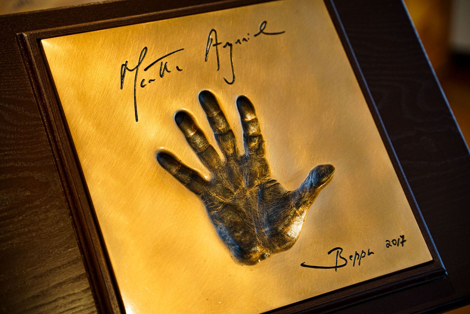 Der Handabdruck von Martha Argerich in Messing gegossen auf einem Holzpanel