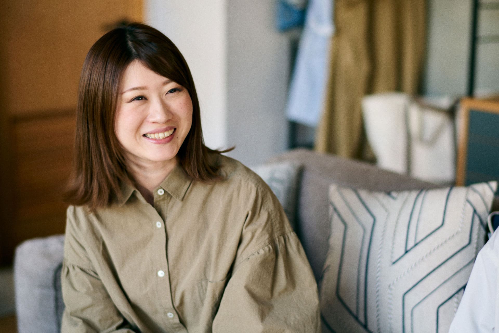 Asami Ogasawara lächelt und sitzt auf einer Couch.