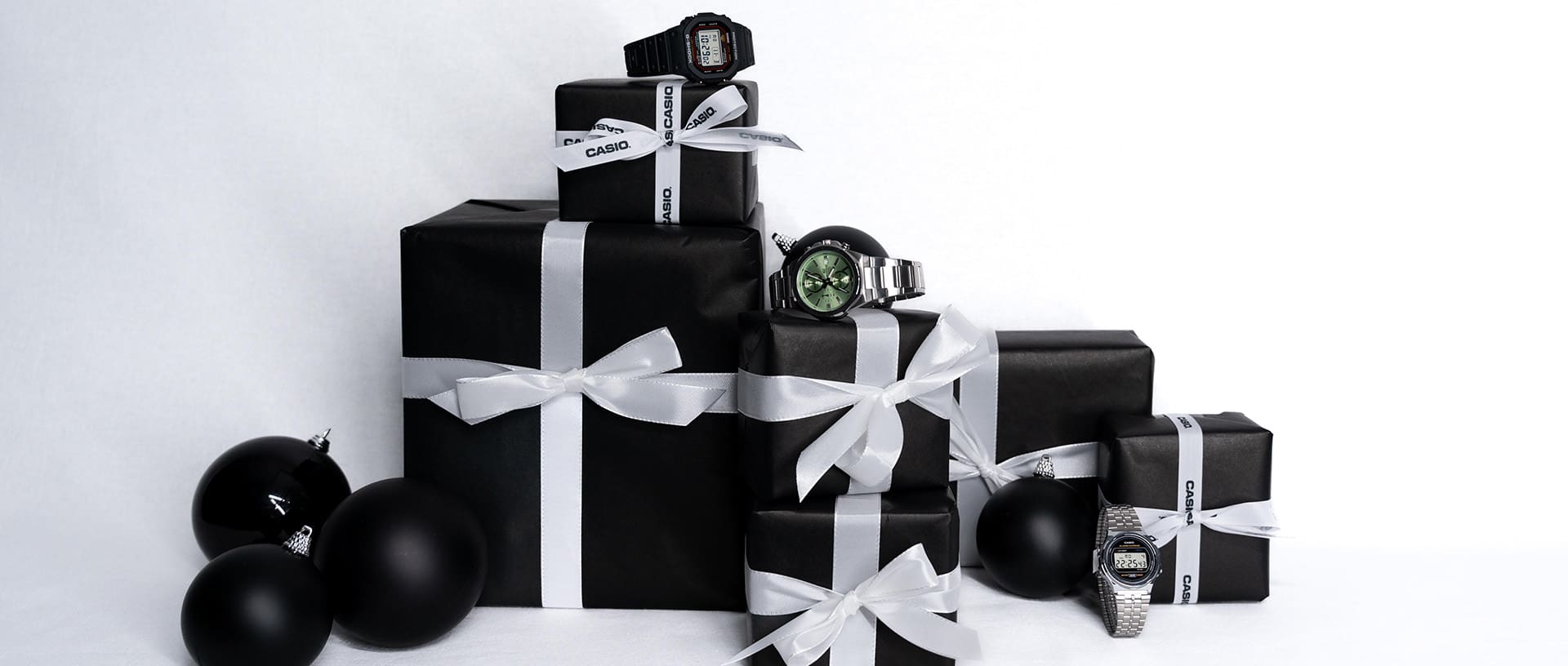 G-SHOCK, CASIO Vintage Collection und Casio Timeless Collection Uhren neben schwarzen Geschenkverpackungen und schwarzen Weihnachtskugeln