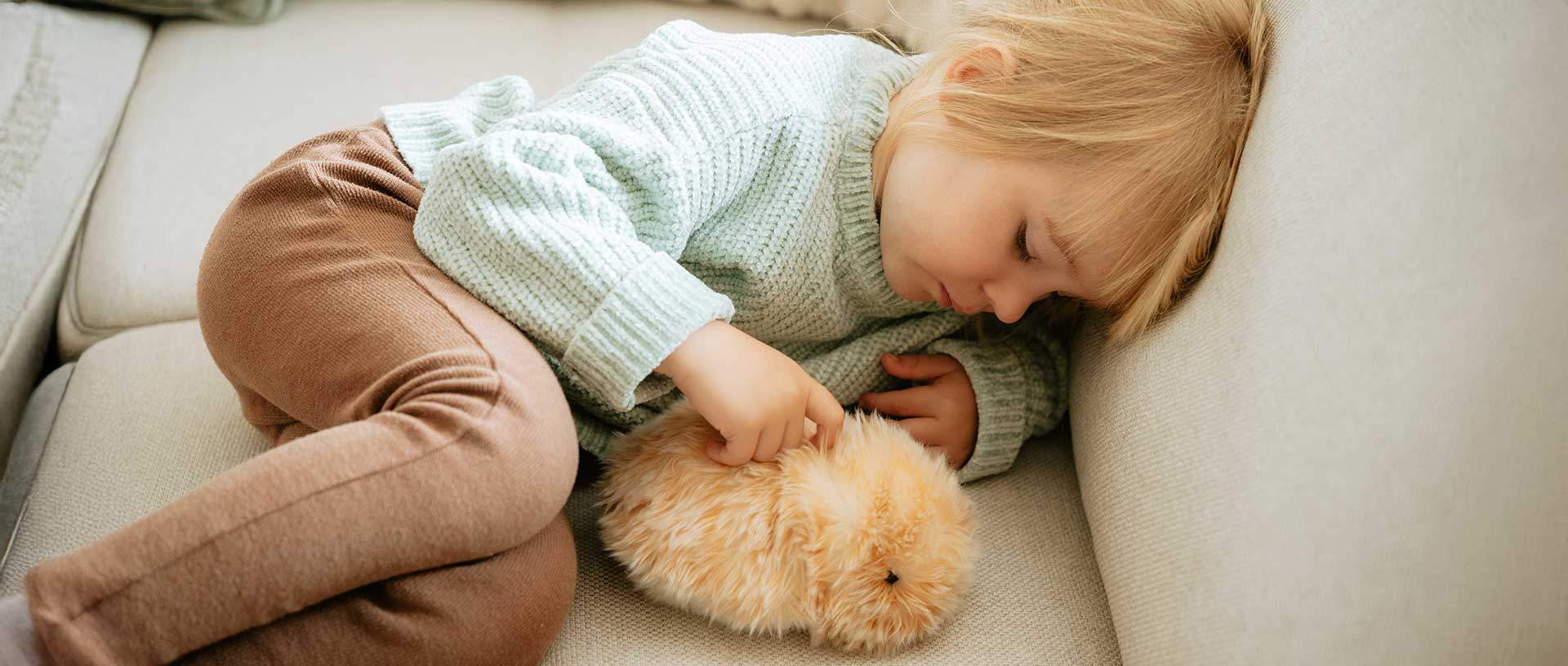 Ein kleines Kind liegt auf einer Couch und kuschelt verträumt mit einem Moflin