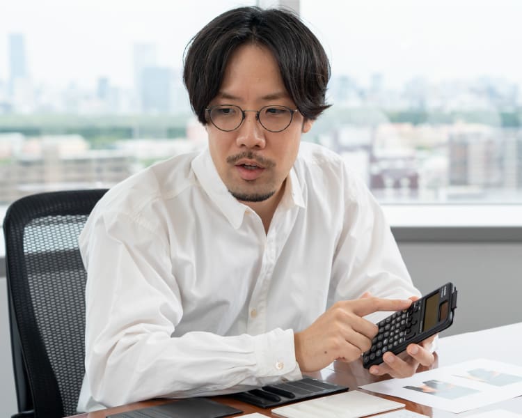 Shunsuke Oka am Schreibtisch mit einem wissenschaftlichen Rechner von CASIO in den Händen