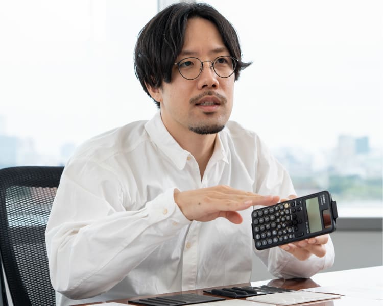 Shunsuke Oka am Schreibtisch mit einem wissenschaftlichen Rechner von CASIO in den Händen
