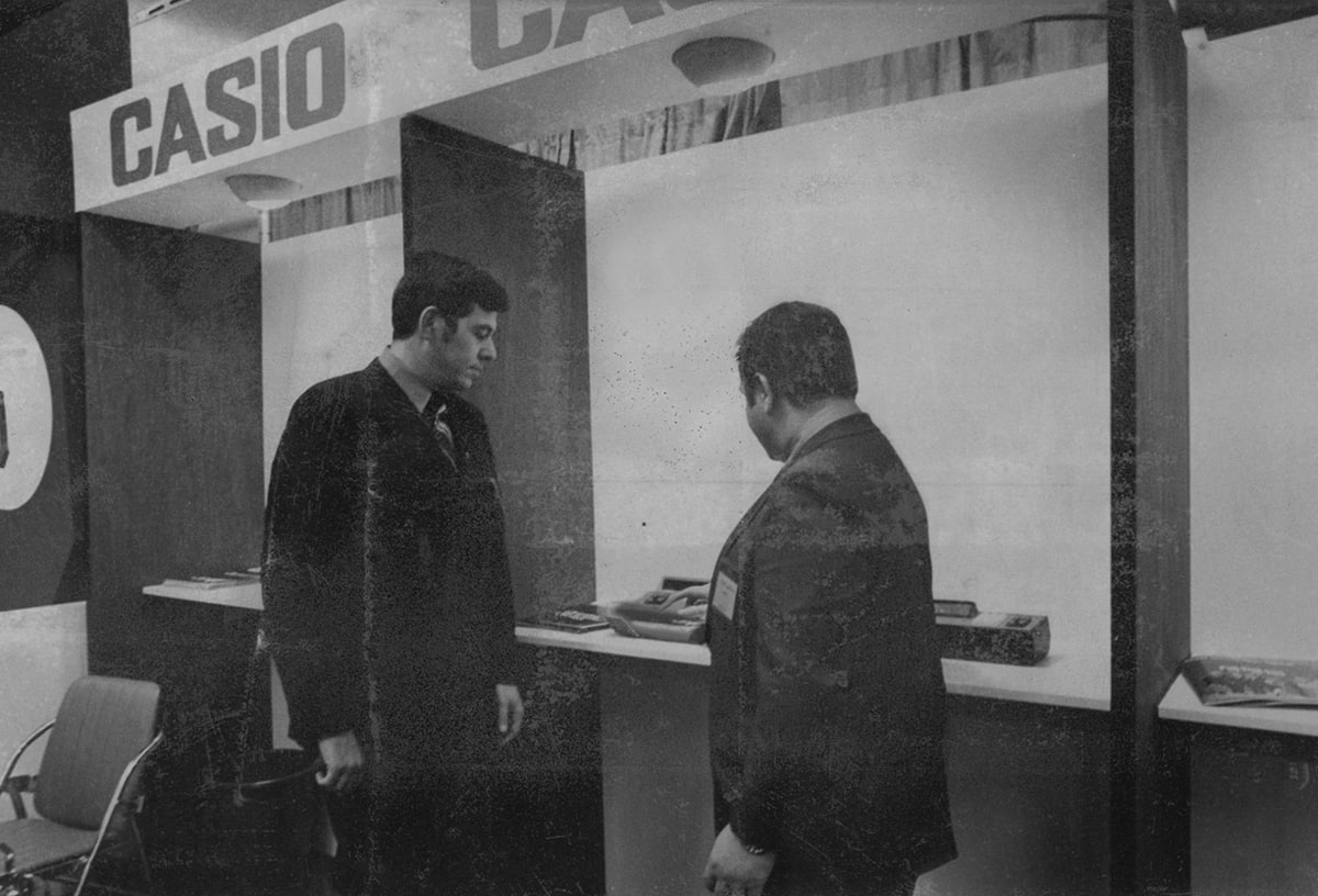 CASIO Messestand bei der Hannover Messe, davor stehen zwei Männer und demonstrieren CASIO Taschenrechner.