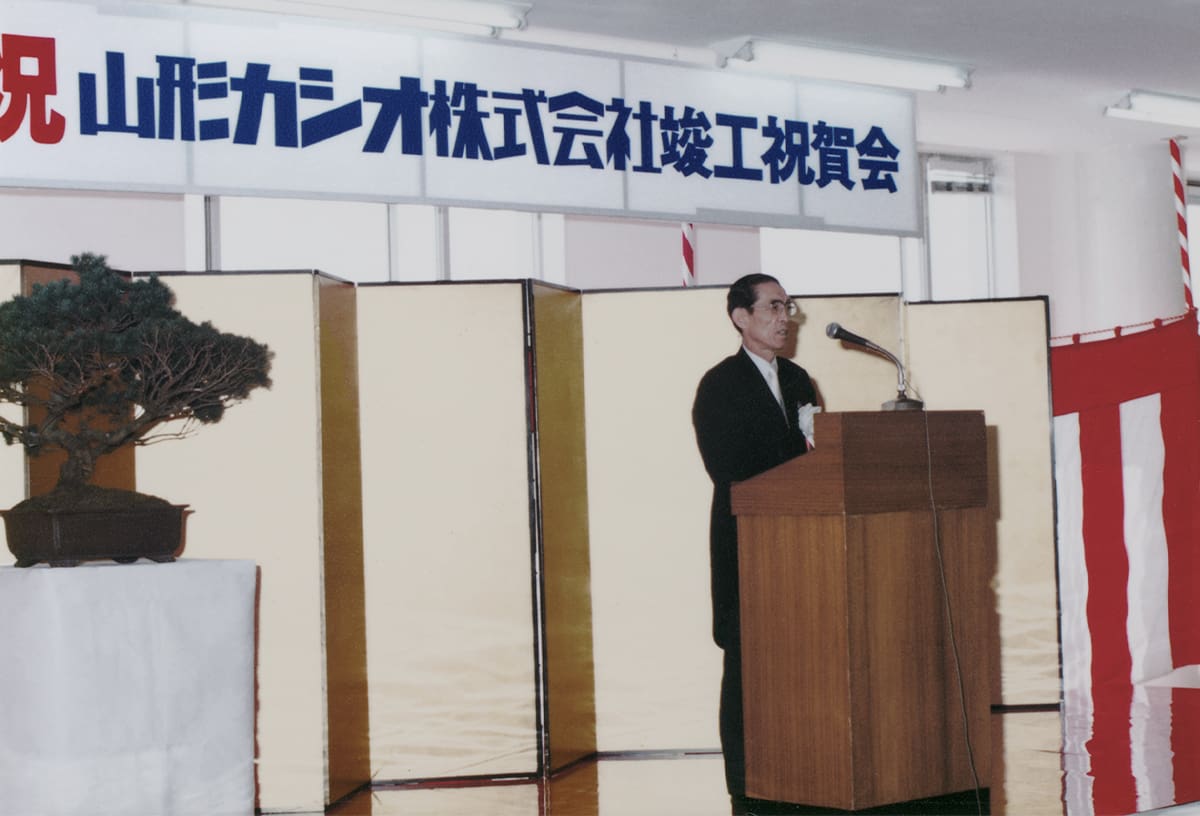 Einer der Kashio-Brüder an einem Redner-Pult bei Gründung des Produktionsstandortes in Yamagata