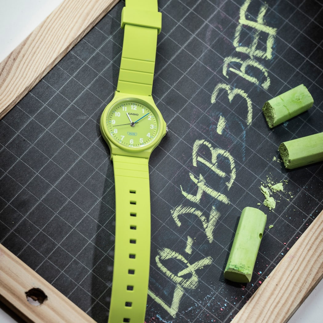 Die hellgrüne CASIO TIMELESS COLLECTION Uhr LQ-24B-3BEF liegt auf einer kleinen Tafel, auf der mit grün der Produktname geschrieben ist.