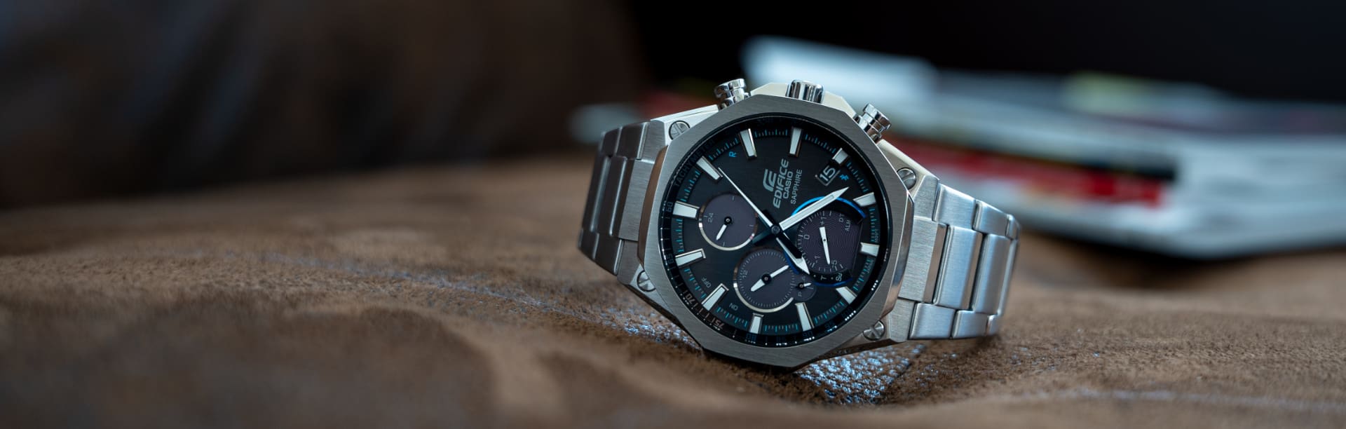Der EDIFICE Chronograph EQB-1100D-1A mit schwarzem Zifferblatt, blauen Details und silberfarbenem Armband auf einem Lederstuhl