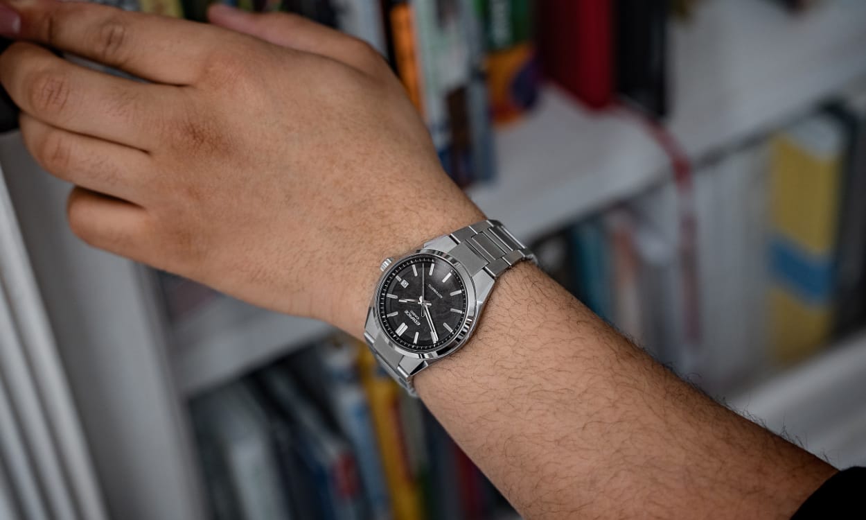 Nahaufnahme der EFK-110 mit dunklem, analogem Zifferblatt am Handgelenk eines Mannes, der nach einem Bücherregal greift