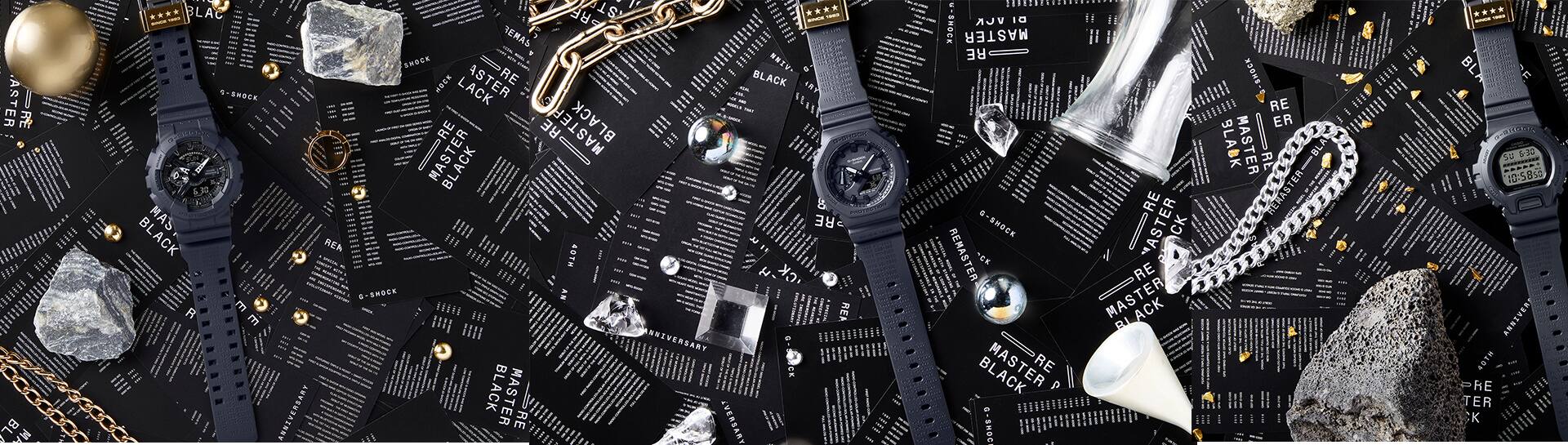 Mehrerer G-Shock Jubiläumsuhren zwischen Steinen, Ketten und Juwelen auf schwarzen Zetteln mit Informationen zu den Modellen