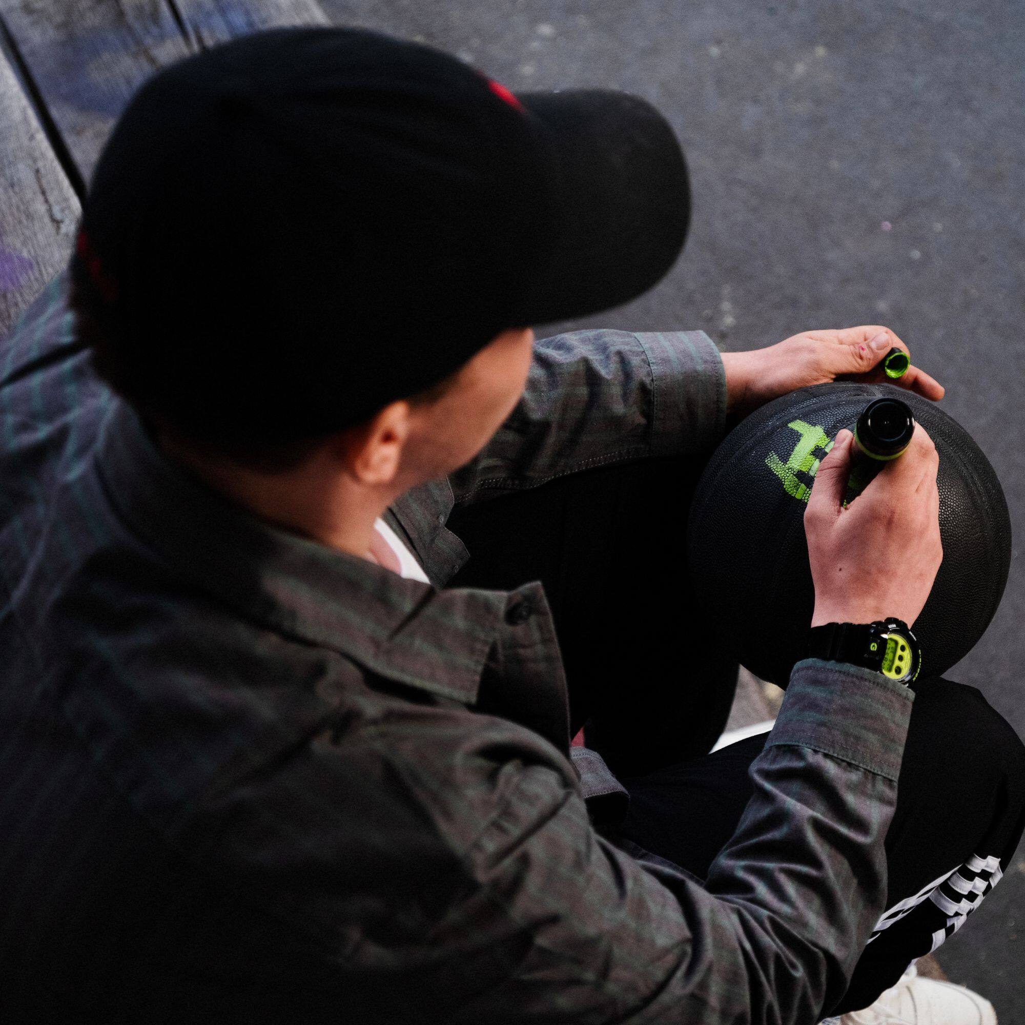 Ein junger Mann schreibt etwas auf einen Basketball, er trägt dabei die schwarze G-Shock DW-6900RCS-1 am Handgelenk. Das Bild verlinkt zur Produktseite.