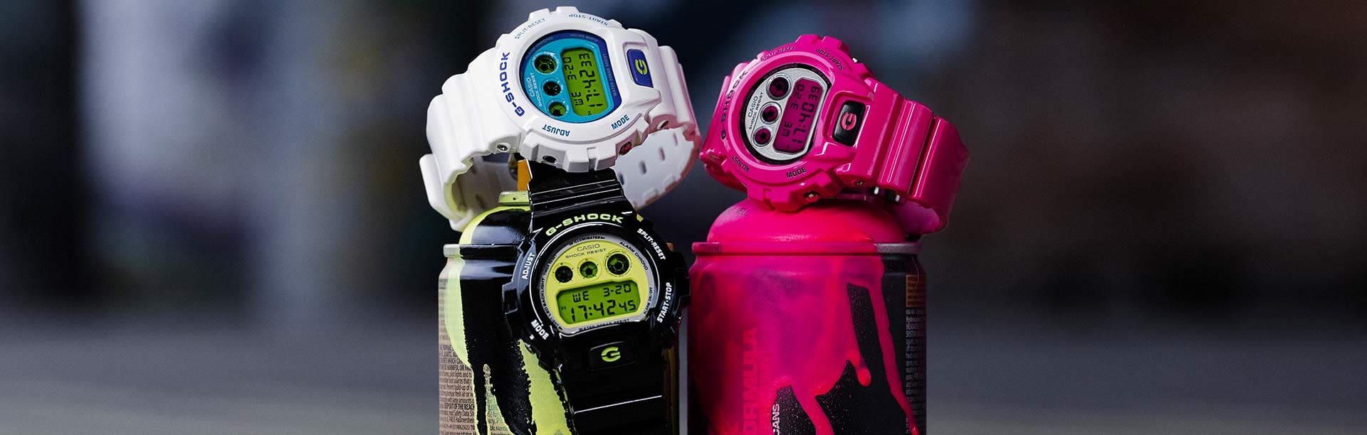 Die drei G-Shock Armbanduhren der Crazy Colour Serie in schwarz, weiß und pink liegen auf Graffitispraydosen.