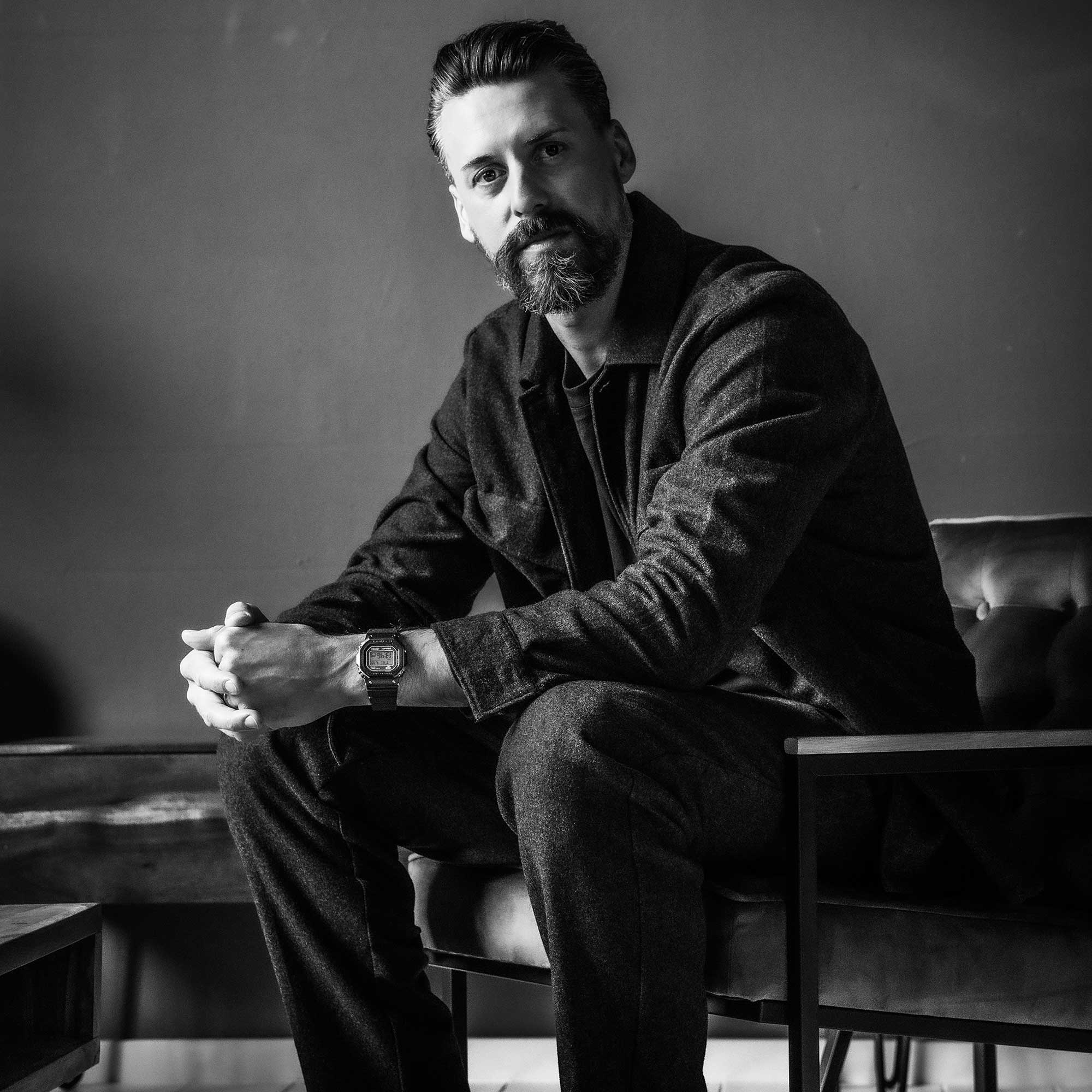 Sandro Wagner sitzt in dunkler Kleidung auf einem Ledersessel und schaut direkt in die Kamera, am Handgelenk trägt er die MRG-B5000R-1 Armbanduhr von G-SHOCK in schwarz, mit digitaler, rechteckiger Anzeige