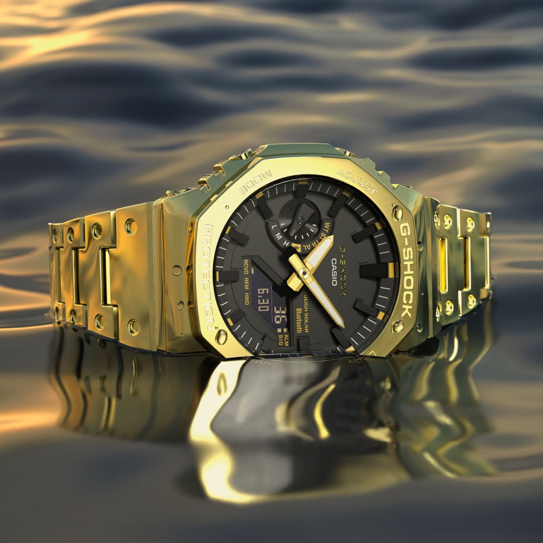 El reloj analógico GM-B2100GD con brazalete de oro flota sobre un fondo acuático