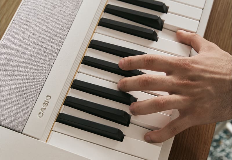 Primer plano de las teclas del piano blanco Casiotone CT-S1-76 mientras una mano toca sobre ellas