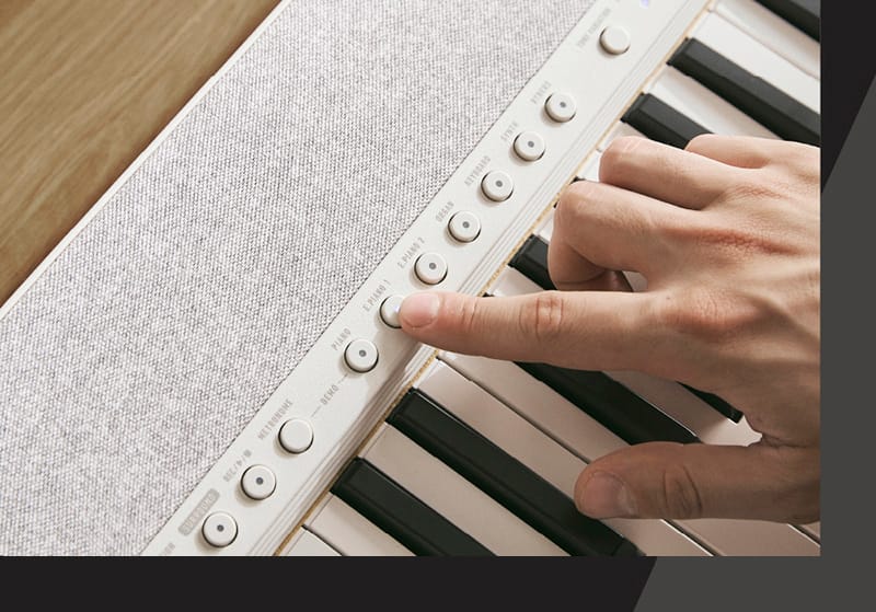 Primer plano del teclado y del panel de control de un  piano digital blanco Casiotone CT-S1-76, un dedo presiona un botón del panel de control