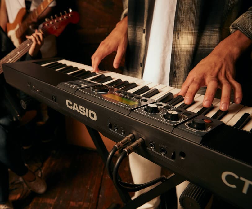 Vista trasera de un Casiotone CT-S500 y sus diversas opciones de conexión, mientras alguien toca el teclado