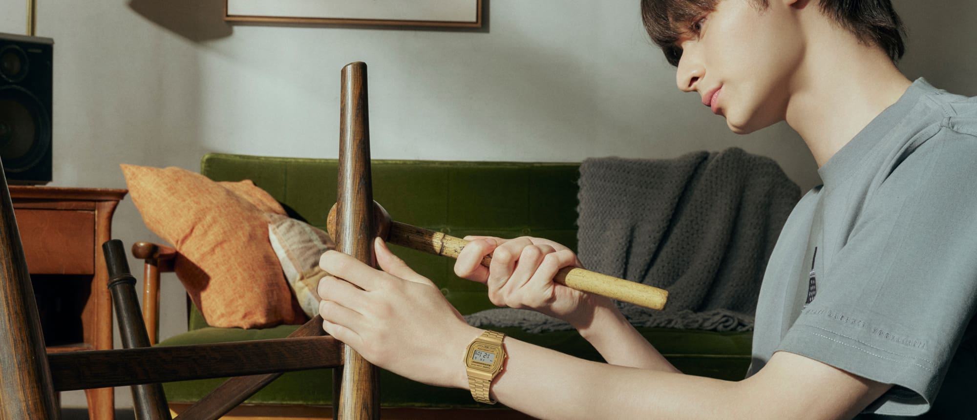 Un hombre repara muebles con herramientas mientras lleva una camisa gris y el reloj CASIO Vintage Collection A168WG-9 con pantalla digital y correa metálica dorada.