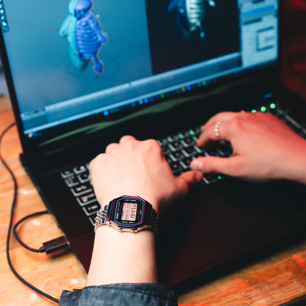 Primer plano de un ordenador portátil en el que se puede ver un modelo 3D, una persona trabajando en él y llevando el reloj digital ABL-100WE en color plateado de la Colección Vintage de CASIO.