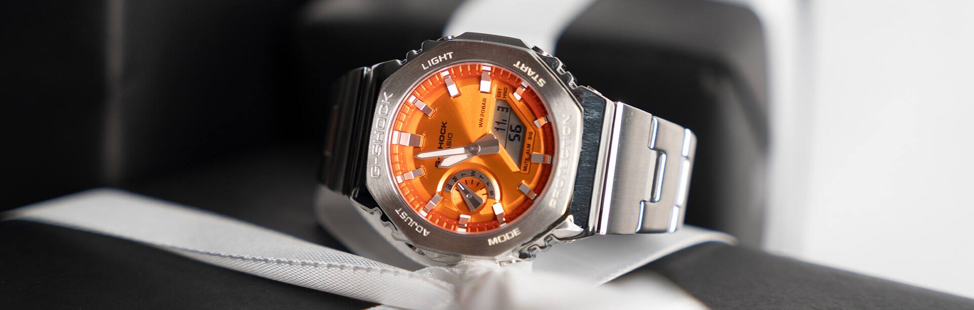 El reloj analógico G-SHOCK GM-2110D-4A con esfera naranja sobre una pila de regalos navideños.