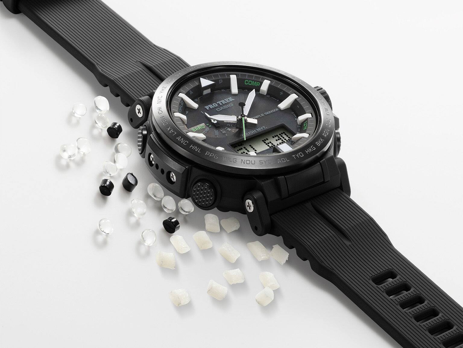 Un reloj negro descansa junto a bolitas negras, blancas y transparentes de resina biológica.